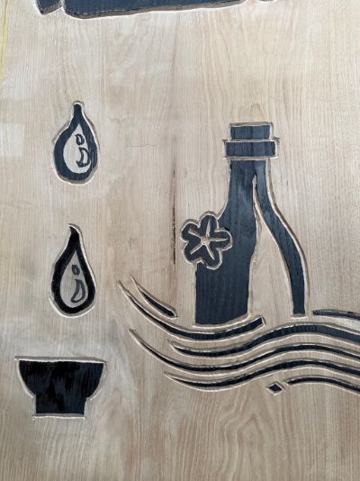 手彫りのロゴ板（酒の字に見立てた瓶と杯の絵）